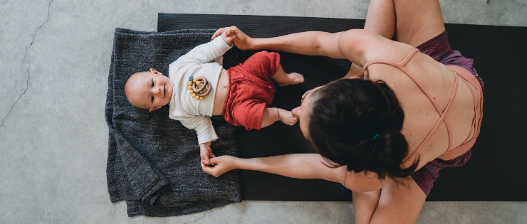 Bird’s eye view of a baby and Mum on a yoga mat at a Mums and Bubs yoga class.