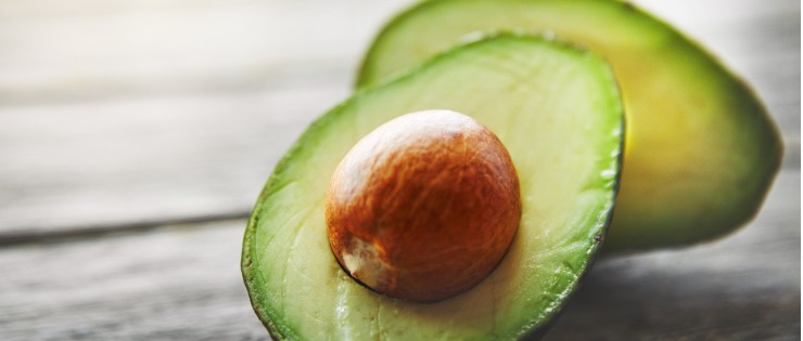 An avocado cut in half, sitting on a wooden table.