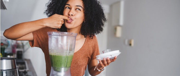 A woman making a superfood green smoothie bowl for breakfast