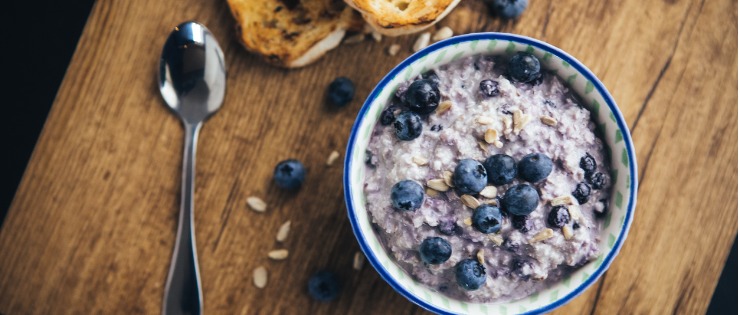 Overnight oats in a bowl topped with blueberries on a wooden chopping board for breakfast.