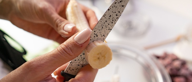 Woman slicing a banana to put on her superfood breakfast smoothie bowl