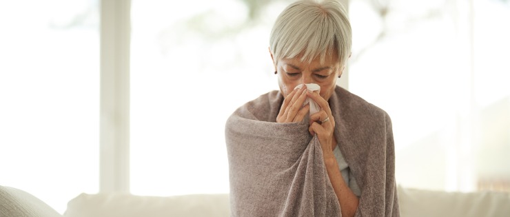 Elderly woman blowing her nose suffering from Flu like symptoms