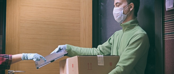 A parcel being delivered at home and receiver signing with a face mask and gloves