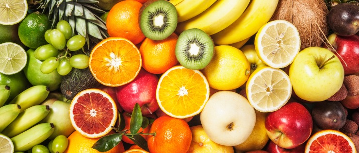 A flat lay of different green, orange, yellow and red fruit on a table.