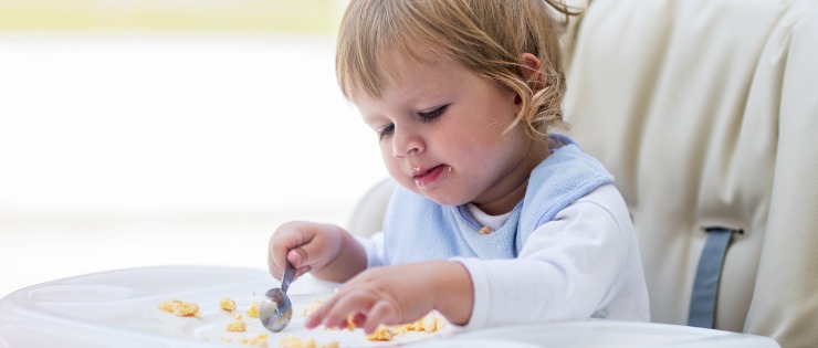 A toddler eating eggs for breakfast in a high chair. 
