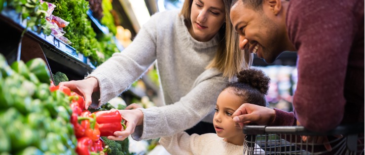 A young girl and her parents picking out fresh vegetables at the supermarket.