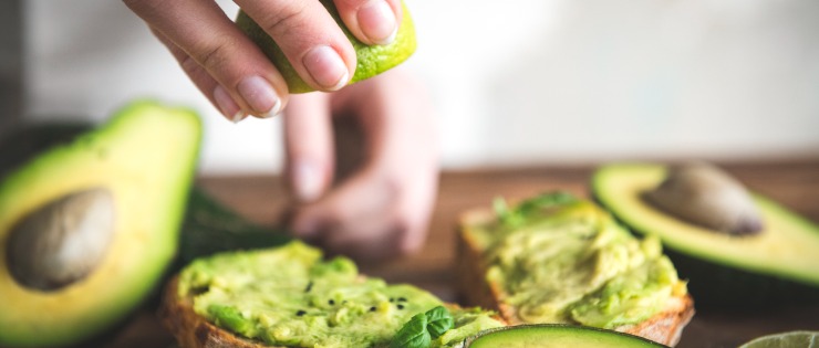The fruit avocado being prepared on toast with a squeeze of lime juice on a wooden chopping board. 