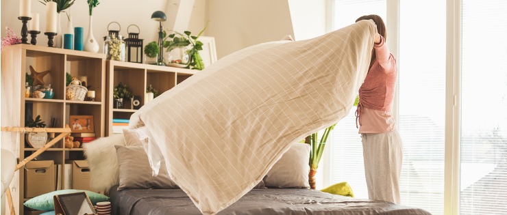 Young woman changing her bed linen to reduce the chance of spreading the flu. 