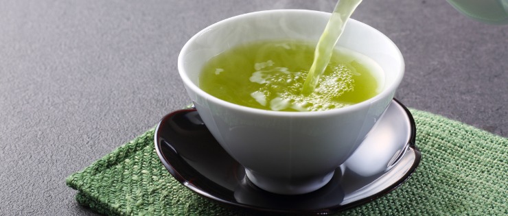 Teapot pouring green tea into small cup