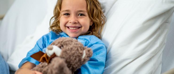 A little girl with private health insurance sitting in her private hospital bed, smiling at the camera.