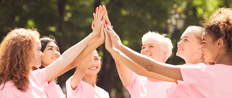 A group of women wearing pink shirts high-fiving each other for breast cancer awareness month.