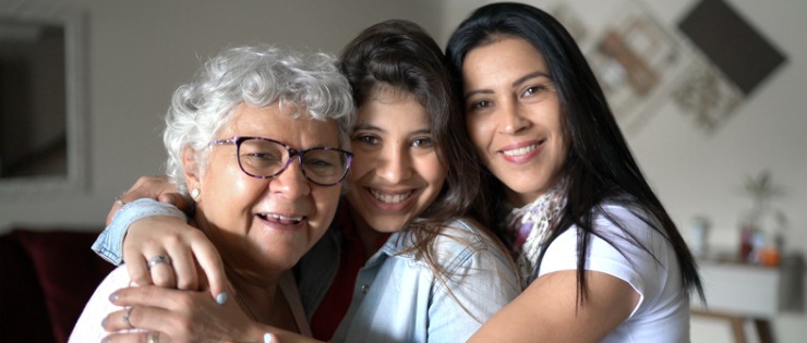 Three generations of women with a history of breast cancer hugging each other in their living room.