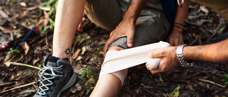 Using a snake bite first aid kit, one person applies a bandage to the injured person's leg